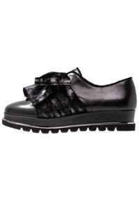 Sneaker nera con punta rotonda, caratterizzata da un ampio fiocco in tessuto e un pannello testurizzato. Suola texturizzata con battistrada distintivo per una buona aderenza.