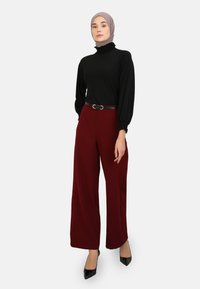 Top negro de manga larga con cuello alto y detalles de volante, combinado con pantalones de tiro alto de pierna ancha en color burdeos y un cinturón negro.