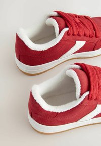 Røde ruskinds sneakers med hvid fleeceforing, der har hvide detaljer og flade snørebånd. Gummisål for godt greb og traction.