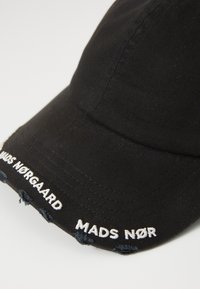 Fekete pamut baseball sapka megkopott szélekkel, fehér hímzett "MADS NØRGAARD" felirattal az elején.
