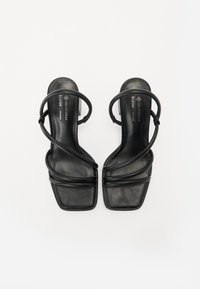 Sandales noires en cuir vegan avec un bout carré plat, dotées de plusieurs fines lanières croisées sur le pied et la cheville pour un maintien sécurisé.