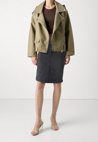 Oliivivihreä tekonahkainen moottoripyöräjakku, jossa on hopeiset yksityiskohdat, yhdistetty tummansiniseen farkkuhameeseen ja kirkkaisiin korkokenkiin.