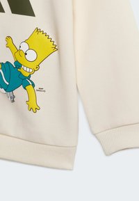 Cream-colored sweatshirt featuring a cartoon character, Bart Simpson, in a blue outfit. Cuffs and hem have ribbed texture.