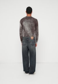 Καφέ, μακρυμάνικο πουκάμισο με υφή και στρογγυλή λαιμόκοψη, συνδυασμένο με φαρδιά, ξεθωριασμένα μπλε τζιν και λευκά αθλητικά παπούτσια, ορατό από πίσω.