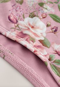 Gros plan sur un tissu rose avec un motif floral blanc et rose et des coutures détaillées le long des bords.