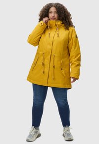 Yellow waterproof parka with a high collar, drawstring waist, and two front pockets. Features wooden toggle accents and a relaxed fit.