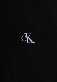 Svart bomullströja med en liten vit broderad "cK"-logotyp. Tyget har en jämn textur och en klassisk rundhalsdesign.