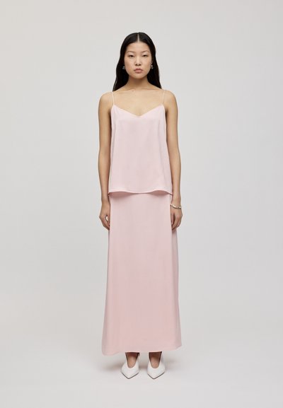 Haut en satin rose clair avec des fines bretelles, superposé à une jupe longue assortie, associé à des escarpins blancs à bout pointu.