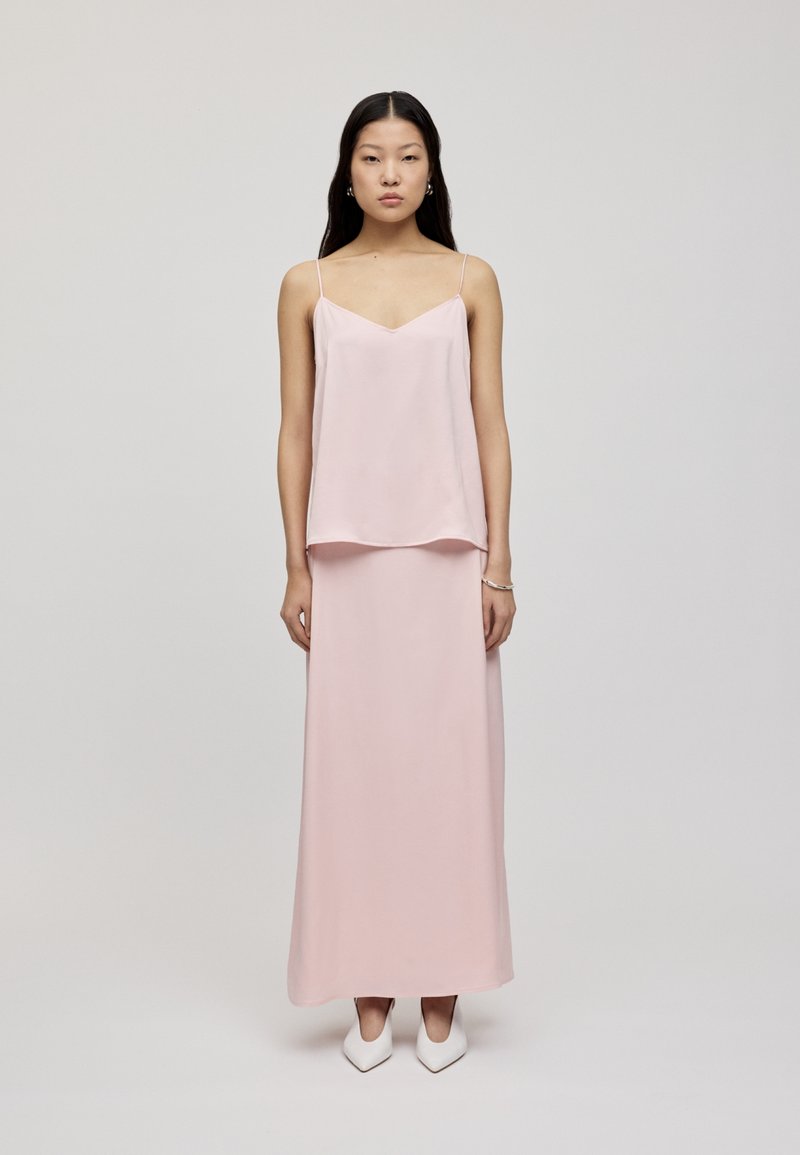 Lys rosa satin cami topp med tynne stropper, lagd over et matchende langt skjørt, parret med hvite spisse hæler.