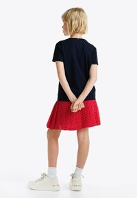 Top navy a maniche corte con colletto rotondo, abbinato a una gonna plissettata a pois rossi. Sneakers bianche con accenti chiari completano l'outfit.