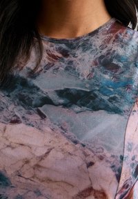 Průsvitný top s abstraktním vzorem v odstínech růžové, modré a hnědé. Kulatý výstřih, měkká textura a poloprůhledný materiál.
