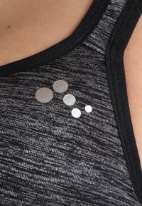 Fekete sportmelltartó texturált, heathered mintázattal. Az elülső bal oldalán sima, lekerekített logó található fényes árnyalatokban.