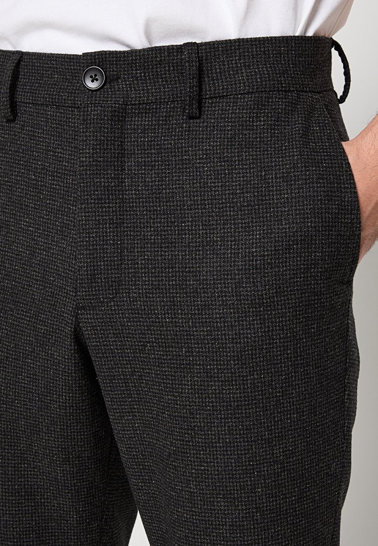 Schwarze, strukturierte Hose mit dezentem karo Muster, ausgestattet mit einem Knopfverschluss, seitlichen Taschen und einer schmalen Passform. Der Stoff hat eine weiche Oberfläche.