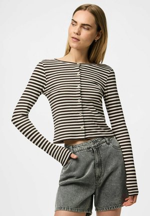 Maglietta a maniche lunghe a righe in marrone scuro e crema con chiusura a bottoni. Indossata con pantaloni corti grigi a vita alta, caratterizzati da una vestibilità comoda.