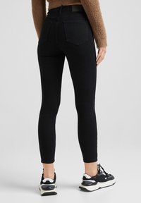 Vaqueros negros ajustados con una textura suave, talle alto y bolsillos traseros clásicos, combinados con zapatillas negras y blancas.