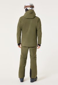 Oliwkowa, wodoodporna kurtka narciarska oraz spodnie, z kapturem, długimi rękawami i czarnymi akcentami na dolnej części nogawek i mankietach spodni.