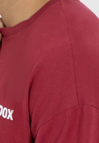 Camiseta color marrón con mangas cortas, cuello redondo y una textura de algodón suave. Presenta una impresión gráfica blanca en la parte delantera.