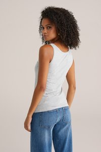 Grå bomullstopp med slim fit, med breda axelremmar och rund halsringning, kombinerad med lösa blå jeans.