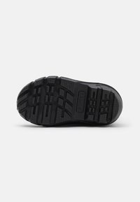 Suela de zapato de goma negra con superficie texturizada, que presenta surcos y patrones distintivos para tracción, con el logotipo en relieve en el lateral.