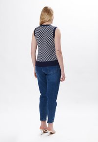 Top senza maniche blu navy e bianco in maglia con motivo circolare; abbinato a jeans in denim blu e sandali con tacco bianchi. Texture liscia, design aderente.