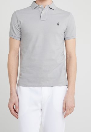 Polo gris de algodón con mangas cortas, un cuello con dos botones y un pequeño emblema negro en el lado izquierdo del pecho.