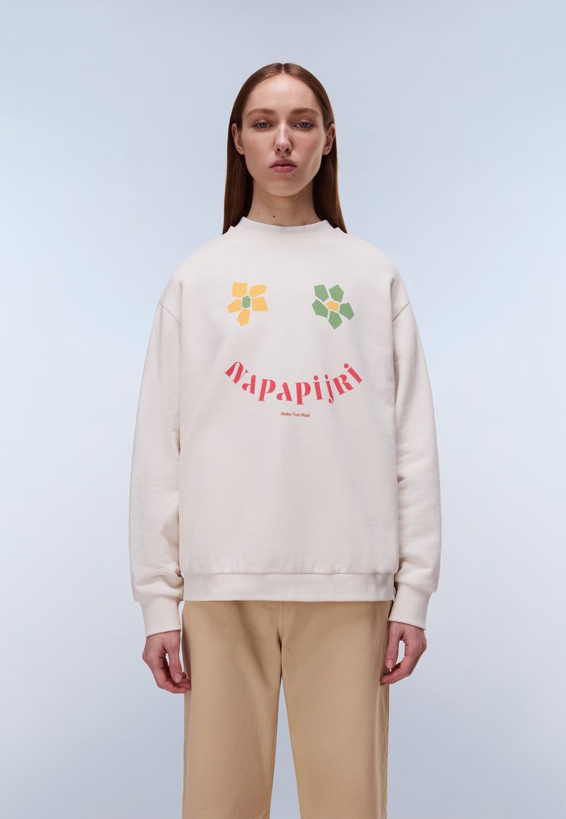 Φόρμα σε ανοιχτό μπεζ χρώμα με στρογγυλή λαιμόκοψη, άνετη εφαρμογή και πολύχρωμα γραφικά λουλούδια σε κίτρινο, πράσινο και κόκκινο, με κείμενο της μάρκας από κάτω.