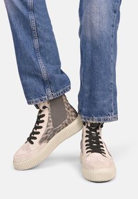 Sneakers typu high-top z jasnoróżowego zamszu, z akcentami w panterkę i szarym bocznym panelem, osadzone na teksturowanej kremowej podeszwie.