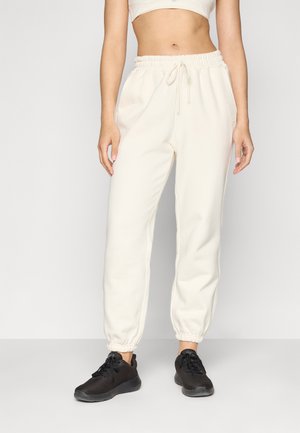 Cremefarvede sweatpants med elastisk talje, snor og manchetter. Båret med sorte, mesh- og gummisålede sportssko.