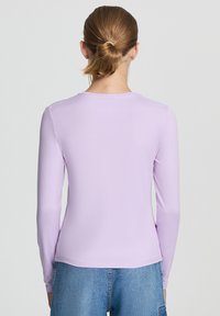 Top a maniche lunghe, aderente, di un leggero colore lavanda, realizzato in un tessuto morbido ed elastico con scollo rotondo e cuciture minime, abbinato a jeans blu di denim.
