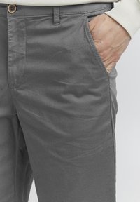 Pantalones de algodón grises con una textura suave, que cuentan con bolsillos laterales y un cierre de botón en la cintura. Diseño simple y ajustado.