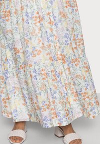 Bloemenmaxi-jurk met een lichte, kleurrijke print van groene, oranje en paarse bloemen op een witte achtergrond; met een tiered zoomontwerp.