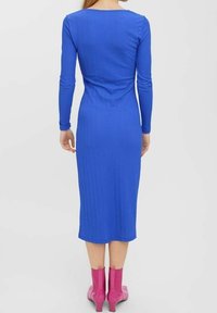 Blau gestreiftes Midi-Kleid mit langen Ärmeln und schmaler Silhouette. Verfügt über einen runden Ausschnitt und reicht bis unter das Knie, kombiniert mit rosa Knöchelstiefeln.