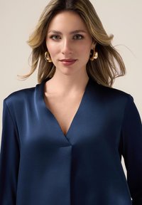 Navy blue satin blouse with a deep V-neck and long sleeves, featuring a smooth texture and minimalistic design.