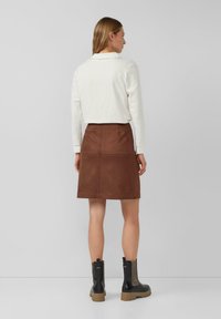 Brązowa zamszowa spódnica o dopasowanym kroju i pionowych przeszyciach. Zestawiona z białą bluzką z długim rękawem oraz czarnymi botkami za kostkę z teksturowanymi akcentami.