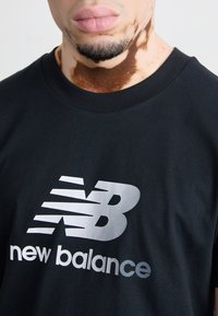 T-shirt nero a maniche corte con un grande logo bianco "new balance". Il tessuto sembra liscio e il collo a giro è a costine.