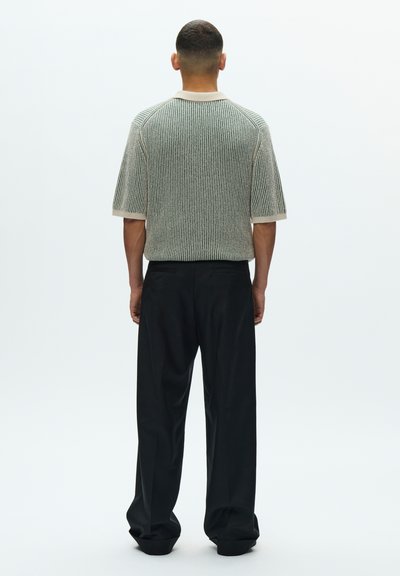 Adīts īsroku tops zaļās, baltās un melnās svītrās ar apaļu kakla izgriezumu, kombinēts ar vaļīgām melnām biksēm. Gluda tekstūra.