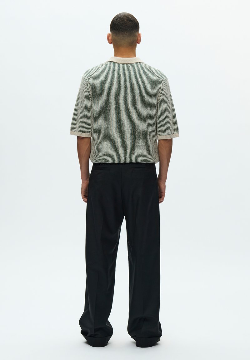 Knitted short-sleeve top in green, white, and black stripes with a crew neckline, paired with loose black trousers. Smooth texture.