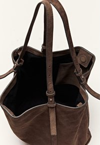 Bruine suède shopper met zwarte binnenkant, lange verstelbare riemen en een binnenvak met een magnetische druksluiting.