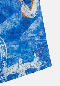 Tessuto grafico blu con motivi astratti, con un'etichetta triangolare "GUESS" all'orlo; la superficie ha una finitura testurizzata.