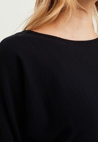 Svart stickad tröja med en bred båthals och mjuk textur, visad delvis för att framhäva tygets detaljer.