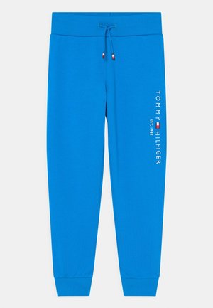 Jasnoniebieskie spodnie dresowe z elastycznymi mankietami i pasem, sznurkiem oraz białym napisem "Tommy Hilfiger EST. 1985" i logo na lewej nogawce.