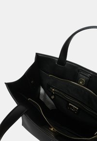 Zwarte leren tote bag met gouden hardware, uitgerust met een binnenvak met rits en insteekcompartimenten voor organisatie. Glad oppervlak.