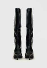 Botas negras hasta la rodilla hechas de cuero suave, con un tacón delgado y un diseño ajustado que presenta una sutil textura arrugada.