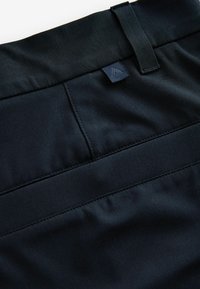 Sorte stofbukser med en flad talje, en label, diskrete syninger og en glat tekstur, med fokus på funktionelle designdetaljer.