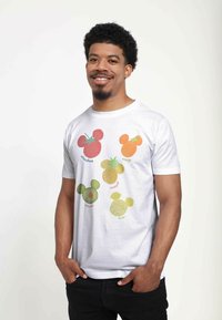 Vit T-shirt med färgglada fruktillustrationer: jordgubbe, apelsin, ananas, avokado och citron i en Mickey Mouse-siluett.