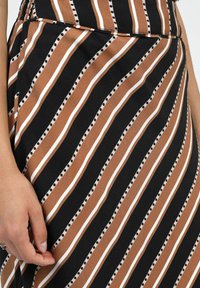 Jupe rayée présentant des couleurs noire, marron et blanche. L'étoffe a une texture lisse avec des rayures diagonales alternées et des accents à pois.