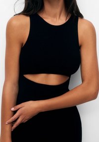 Top senza maniche nero a coste, caratterizzato da un colletto alto e un dettaglio cut-out in vita. Il tessuto ha una texture liscia e un design aderente.