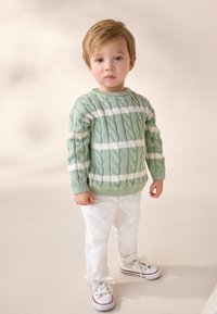 Green cable-knit sweater with white stripes, paired with white pants and white sneakers featuring red and blue accents. Simple, textured design.