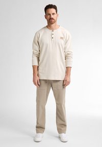 Crème overhemd met lange mouwen en een henley-halslijn met drie knopen, gecombineerd met lichtbeige cargo broeken met twee voorzakken.