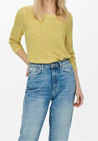 Maglione giallo a maglia con collo rotondo e maniche a tre quarti, abbinato a jeans a vita alta di colore blu chiaro e taglio dritto.